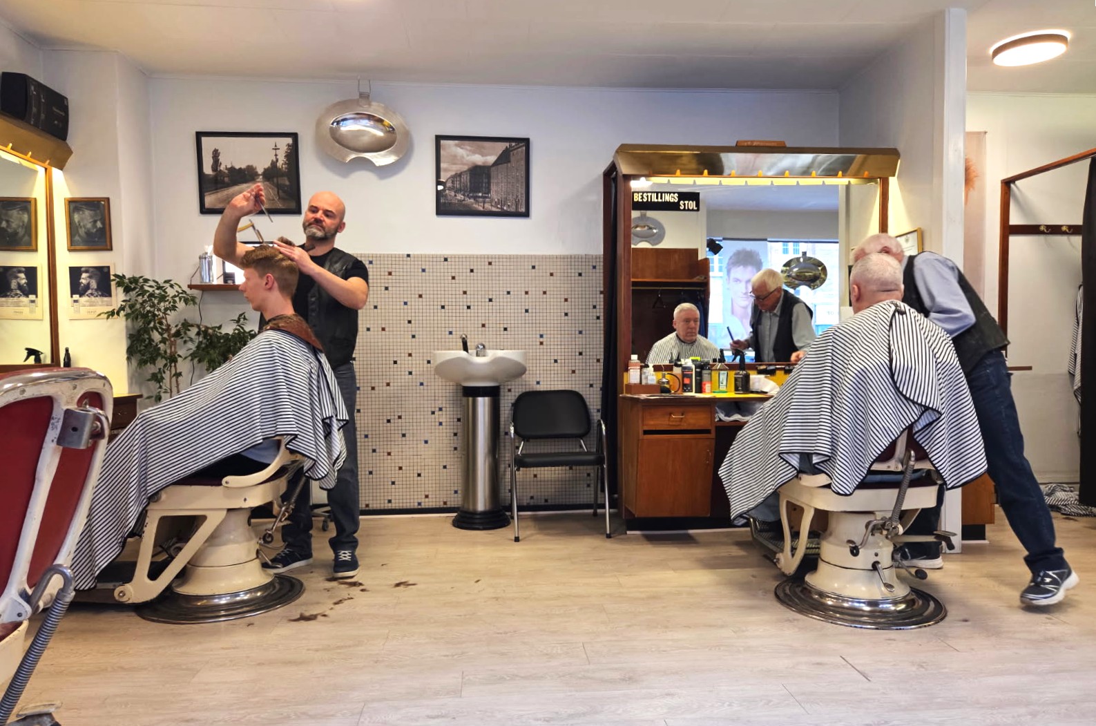 Den over 100 år gamle herrefrisør på Peter Bangs vej i afdeling 11 på Frederiksberg - Her ses et billede af ejeren, Bayram, og Arne der har kunder i frisørstolene.
